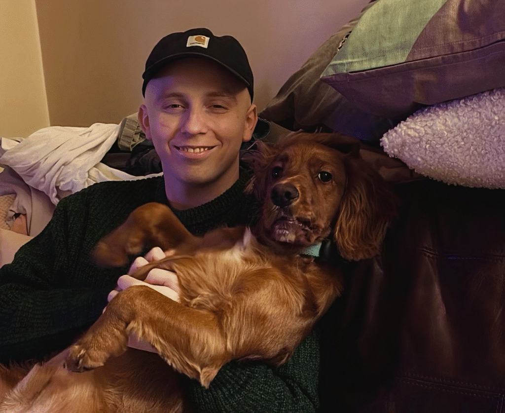 Man sitting on the sofa smiling at camera, with a dog laying on his chest