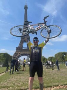 A man stands in front of the Eiffel Tower holding his bike in the skky