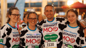 Three women and one man stand in a row smiling at the camera. They are dressed in cow print t-shirts.
