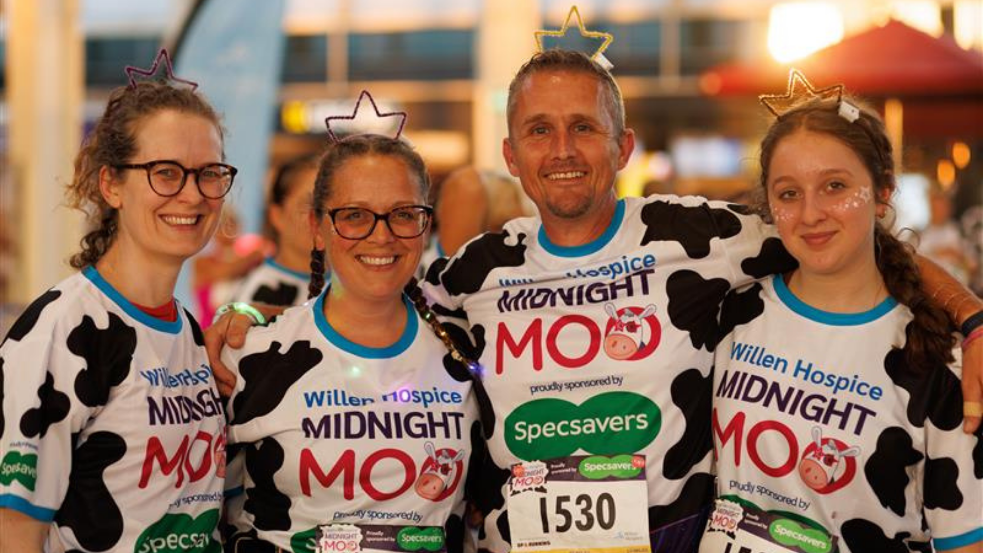 Three women and one man stand in a row smiling at the camera. They are dressed in cow print t-shirts.