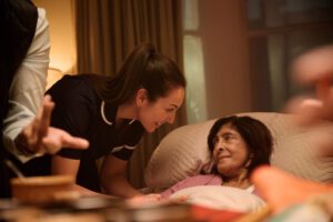 Lady lying in bed with a nurse learning over to speak to her.