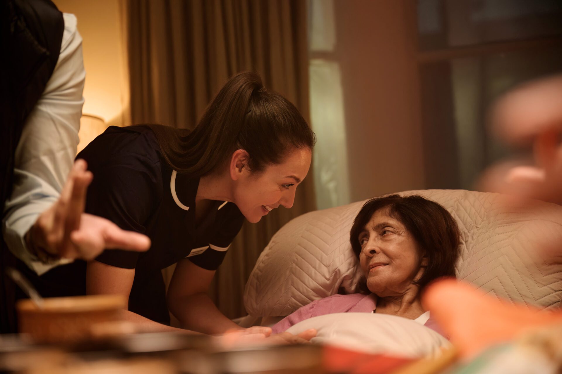 Lady lying in bed with a nurse learning over to speak to her.