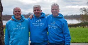 Three men standing outdoors smiling for camera with a lake in the background