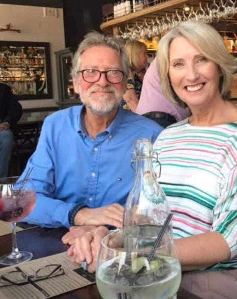Man and woman smiling at camera with drinks on the table in front of them