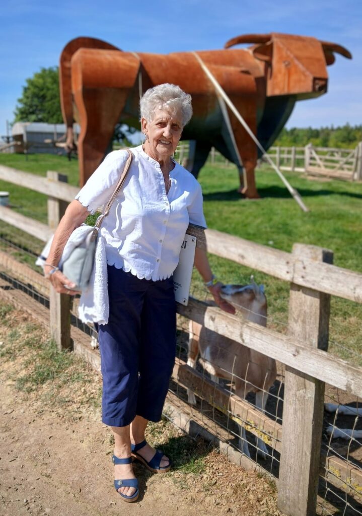 Older woman outside smiling at camera with cow sculpture in background