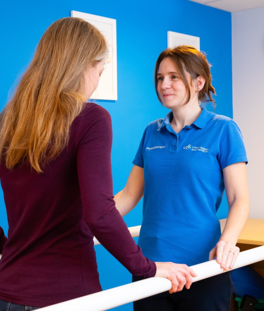 Physiotherapist helping person to walk leaning on parallel bars